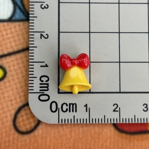 Macro shot of tiny yellow resin bell with red bow on a measuring board for nail art
