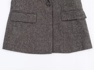 Detail of dark grey herringbone wool blazer showing symmetric flap pockets and fabric texture