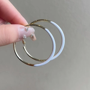 Detail shot of large gold and white enamel hoop earrings held in hand for scale