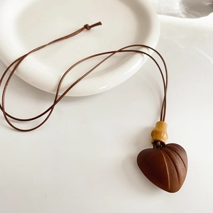 Detailed view of a brown wooden heart pendant necklace with a braided cord on a white plate