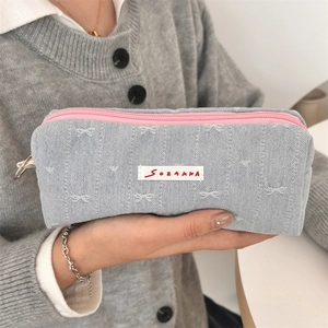 Detailed close-up of light blue denim bow pencil case with pink zipper held in hand