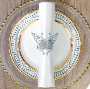 Close-up of silver hollow butterfly napkin ring on white linen and elegant plates