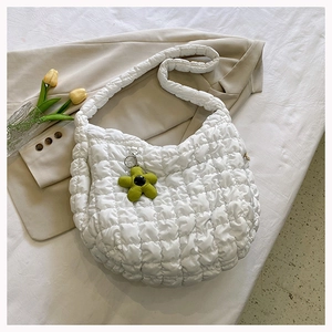 Detail of white quilted puff tote bag with green flower charm on a neutral bedding