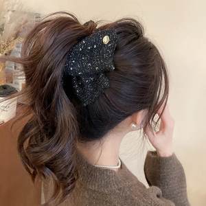 Black tweed bow hair clip with gold logo button on model for an elegant hair look