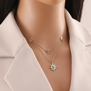 Detail of gold layered necklace with tree of life charms and turquoise sun pendant on model