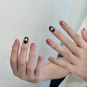 Close-up of oval press-on nails with black and pink heart patterns and glitter accents