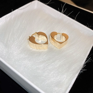 Detailed view of golden heart-shaped hoop earrings with engraved text in a plush box