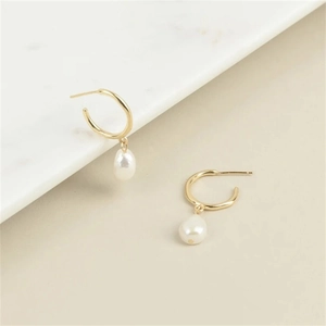 Macro view of gold hoop earrings with white baroque freshwater pearls on marble
