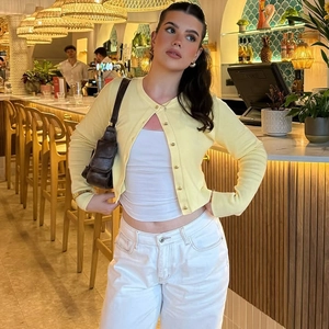 Détail d'un gilet en maille jaune clair avec boutons et manches longues dans un café