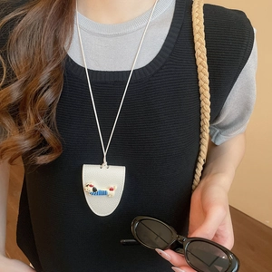 Close-up of a white shield-shaped leather pendant with a cartoon dog and long neck strap