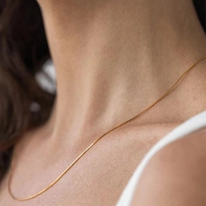Close-up of a delicate 18K gold snake chain necklace worn by a model for a refined look