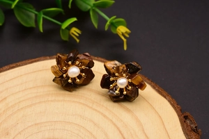 Macro detail of handmade floral stud earrings with tiger eye petals and white pearl center