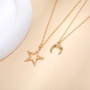 Detail of two gold star and crescent moon pendant necklaces on a soft beige background