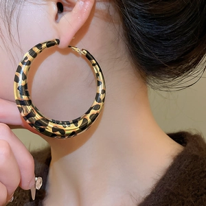 Close-up of a large gold leopard print hoop earring worn by a model in a side view