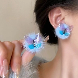Detail of blue faux fur pompom earrings with a gradient resin butterfly accent