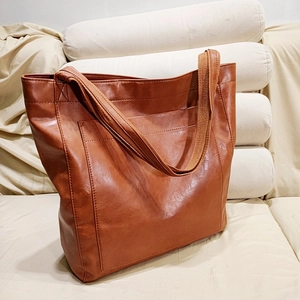 Gros plan d'un sac cabas marron en similicuir avec poche frontale sur un canapé beige