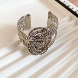 Detailed close-up of multi-layer silver woven metal chain bracelet on a wave tray