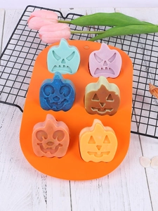 Macro view of a 6-cavity orange silicone mold with colorful pumpkin soaps on white wood