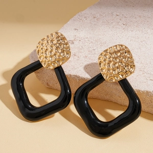 Detail of geometric earrings with golden hammered texture and black resin square hoop