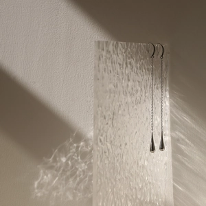 Silver long tassel earrings with teardrop pendants against water-textured glass backdrop