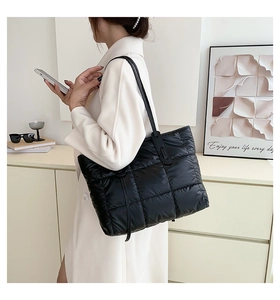 Side view of a large black quilted tote bag with puffer texture worn on shoulder