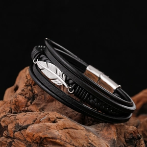 Close-up of multilayer leather bracelet with silver feather pendant on rustic wood