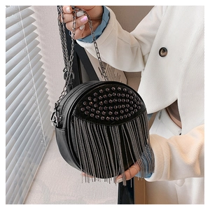 Close-up of black round leather bag with punk studs and long metal fringe details