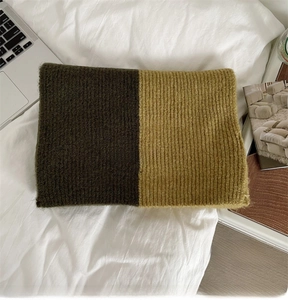 Close-up of knit scarf texture in olive green and mustard yellow with white fabric label
