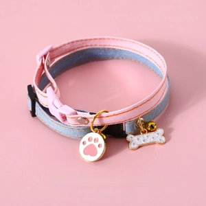 Close-up of pink and blue canvas pet collar with bell and bone pendants on pink background
