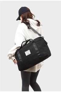 Model wearing a black quilted travel bag with diamond patterns and adjustable strap