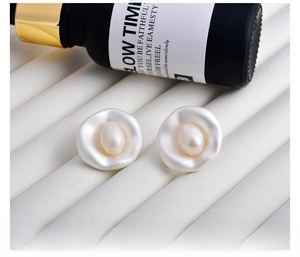Detail of baroque pearl earrings with irregular petal edges on white leather stand