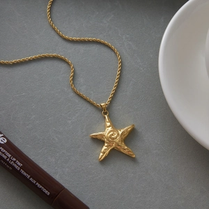 Macro shot of gold starfish pendant with detailed texture on twisted rope chain