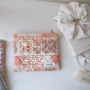 Pochette en tissu matelassé avec motifs floraux et lapins sur fond blanc épuré