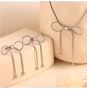 Detailed view of silver bow-shaped necklace and earrings set on a warm beige background