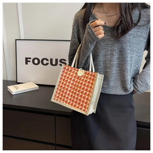 Detail of red and orange woven jute tote bag with wooden button closure and beige handle