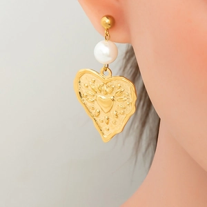 Close-up of textured gold heart earring with a round pearl bead on a model's ear