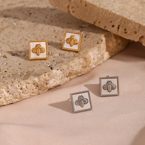 Detail of square bee earrings in gold and silver finish on natural stone background