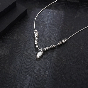 Silver snake chain necklace with leaf pendant and geometric beads on black surface
