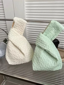 Close-up of white and green knotted wrist bags with unique embossed pleated texture