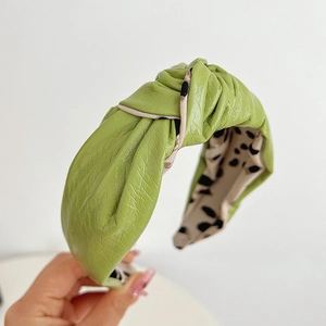 Detail of green knotted headband featuring a glossy leather-like finish and spotted lining