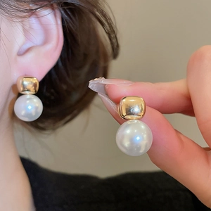 Close-up of gold square stud earrings with dangling white round pearls for women