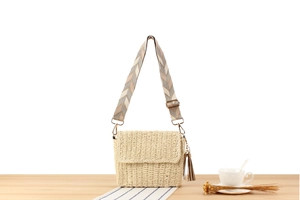 Detail of hand-woven beige crossbody bag with patterned strap on wooden surface