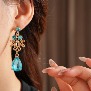 Detailed view of vintage gold hollow earrings with blue teardrop gems on a model