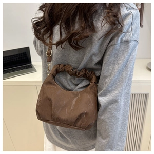 Detail einer braunen Schultertasche mit Raffgriff, getragen von einem Modell