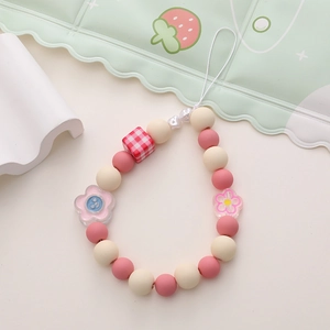 Detailed view of pink and cream beaded phone charm with red checkered bead and floral pendant