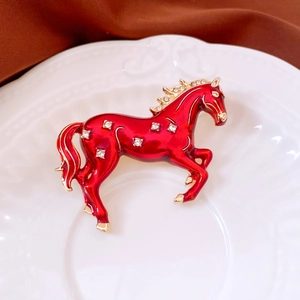 Detailed close-up of a vintage golden horse brooch with red enamel and sparkling rhinestones