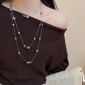 Detail of layered silver flower and cross pendant necklace with white crystals on model