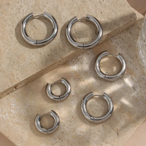 Three pairs of shiny silver minimalist hoop earrings in various sizes on a stone surface