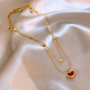 Detail of double-layer gold necklace with red heart pendant on grey silk fabric