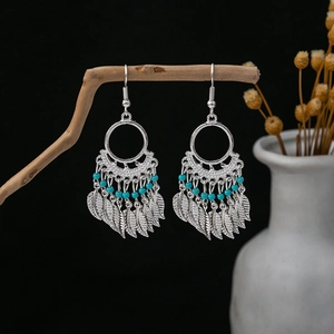 Detail of Bohemian silver leaf earrings with blue beads hanging on a rustic wooden branch
